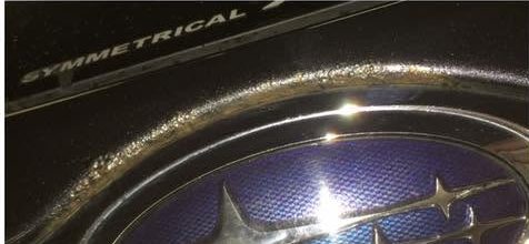 Close up of paint blistering and corrosion breaking through along the boot lid of a dark grey Subaru